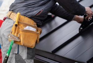 Roofer with a tool belt fitting a dark metal roof panel