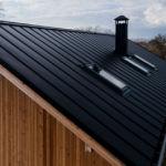 Black standing seam metal roof with skylights and a chimney on a cedar-clad house