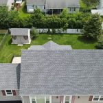 Aerial view of a one-storey house with a grey asphalt shingle roof, a backyard shed and a fenced lawn.
