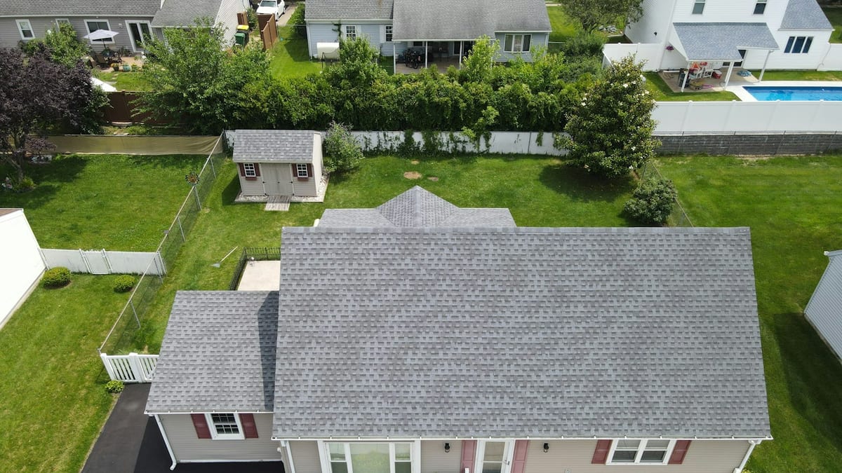 Aerial view of a one-storey house with a grey asphalt shingle roof, a backyard shed and a fenced lawn.