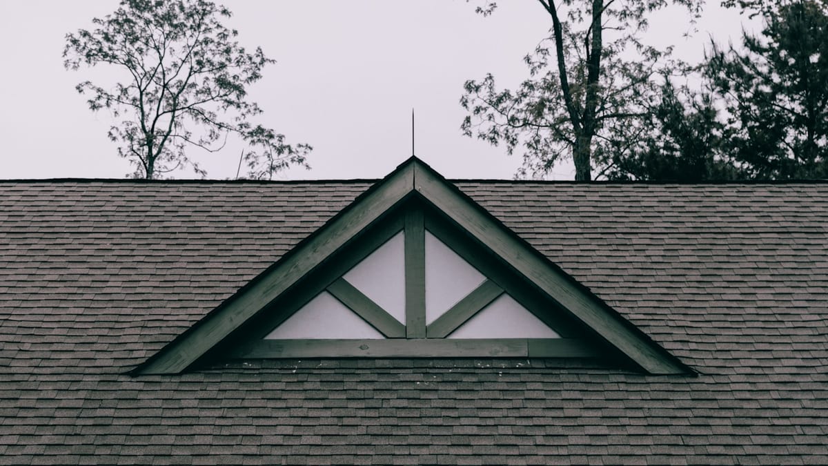 Dark asphalt shingles laid in even courses around a gable vent with green trim.