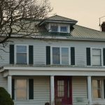 Two-storey white farmhouse with a green metal roof over the front porch and entry door.