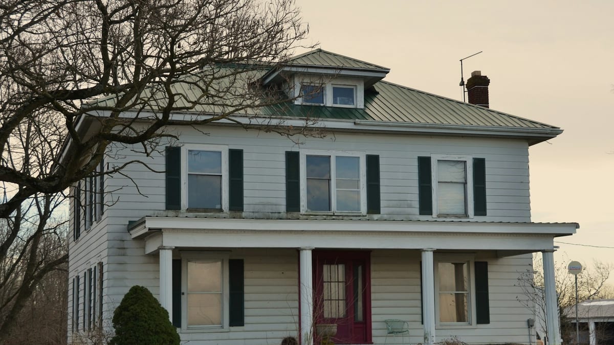 Two-storey white farmhouse with a green metal roof over the front porch and entry door.
